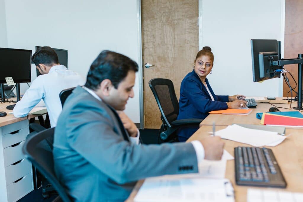 3 people working in an office speaking to each other across their work desk.